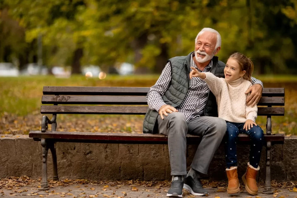 Grandfather and young girl sitting on park bench.